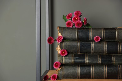 Photo of Stack of books and beautiful flowers on shelf near grey wall. Space for text