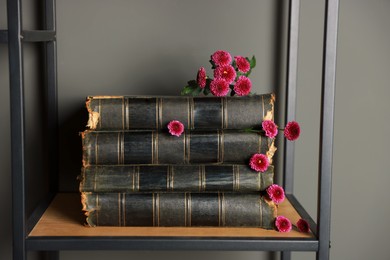 Stack of books and beautiful flowers on shelf near grey wall