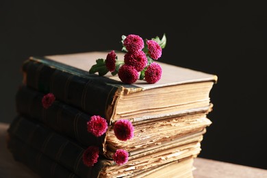 Stack of books and beautiful flowers on table against black background, closeup