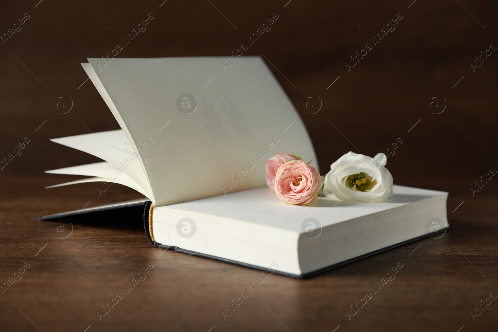 Photo of Open book with beautiful flowers on wooden table, closeup