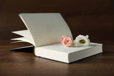 Photo of Open book with beautiful flowers on wooden table, closeup