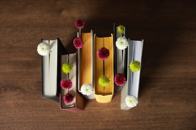 Photo of Different books with beautiful flowers on wooden table, above view