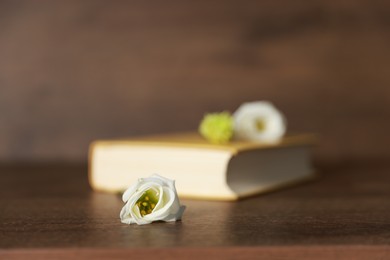 Photo of Beautiful flower bud and book on wooden table, selective focus