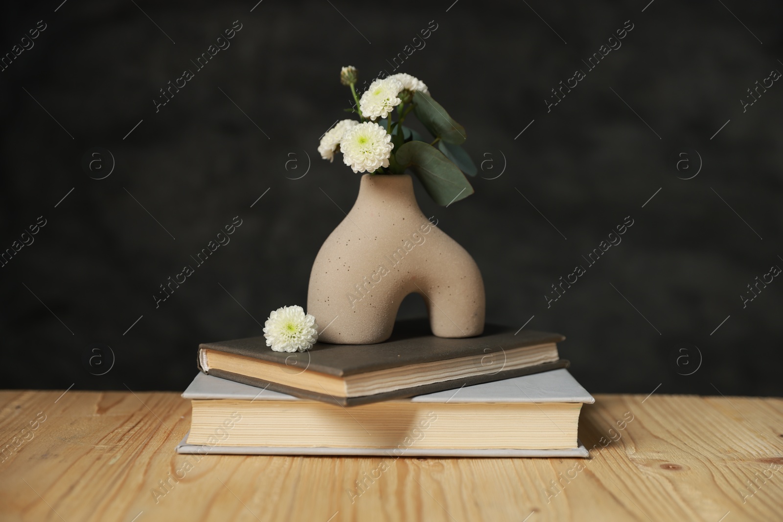 Photo of Books and decorative vase with beautiful flowers and eucalyptus branches on wooden table against black background, closeup