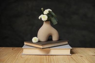 Books and decorative vase with beautiful flowers and eucalyptus branches on wooden table against black background, closeup