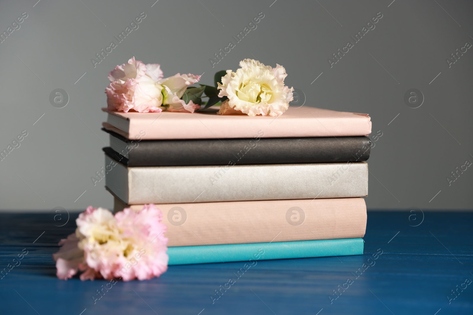 Photo of Stack of books and beautiful flowers on blue wooden table against grey background, closeup