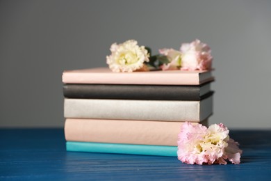 Stack of books and beautiful flowers on blue wooden table against grey background, closeup