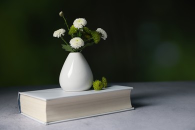 Photo of Book and vase with beautiful flowers on grey textured table against blurred background, closeup