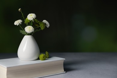 Book and vase with beautiful flowers on grey textured table against blurred background, closeup. Space for text