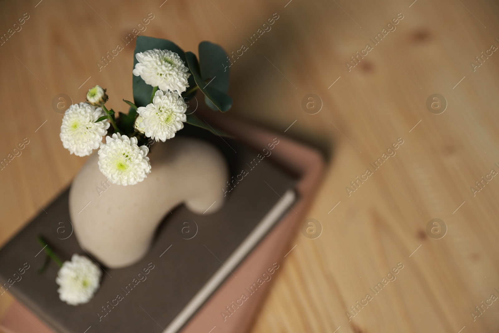 Photo of Books and decorative vase with beautiful flowers and eucalyptus branches on wooden table, closeup. Space for text