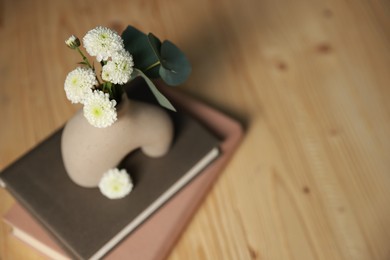 Photo of Books and decorative vase with beautiful flowers and eucalyptus branches on wooden table, closeup. Space for text