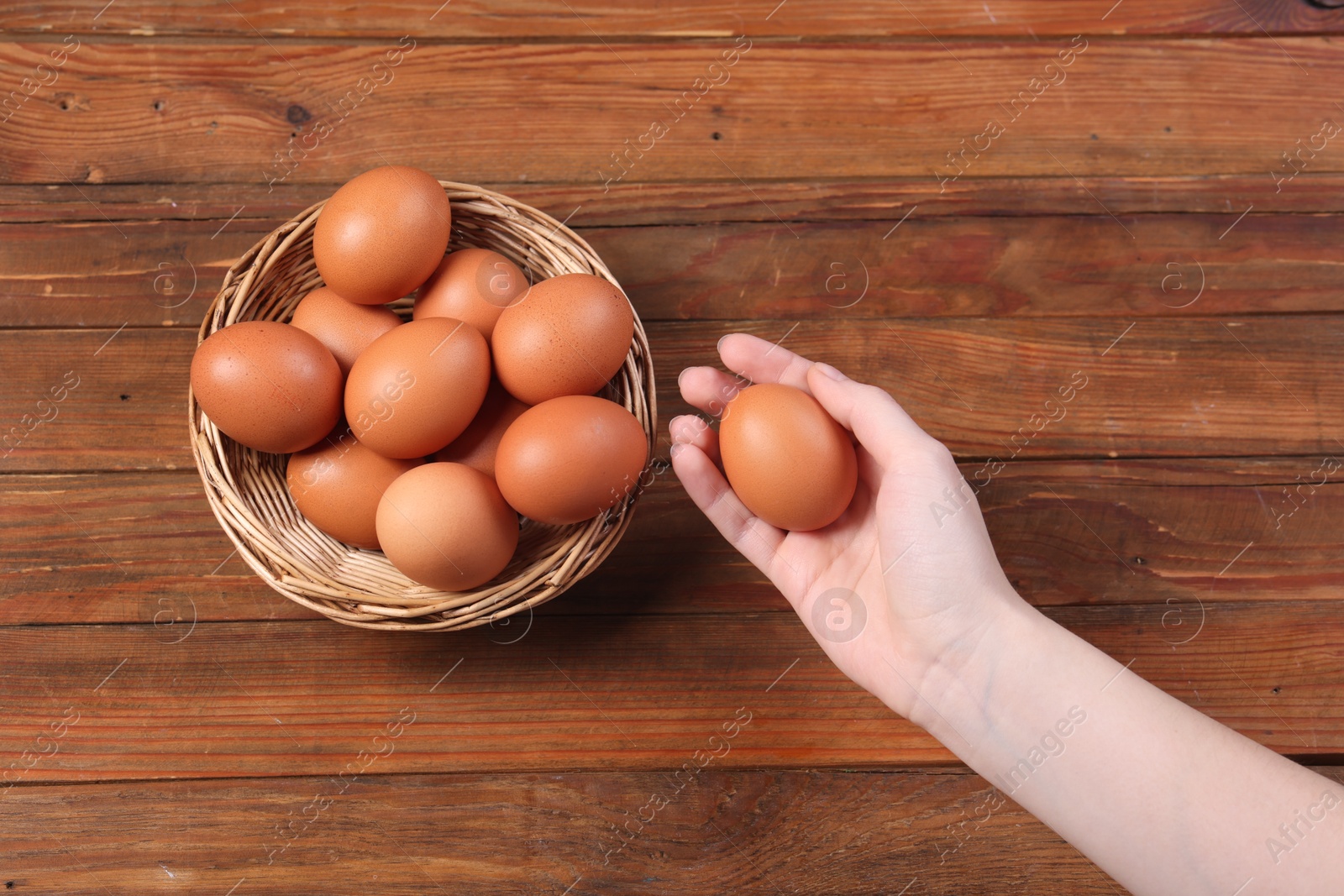 Photo of Woman with raw eggs at wooden table, top view