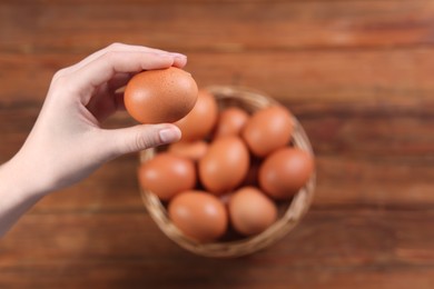 Photo of Woman holding raw egg above wooden table, closeup