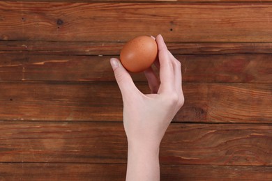 Photo of Woman with raw egg at wooden table, top view