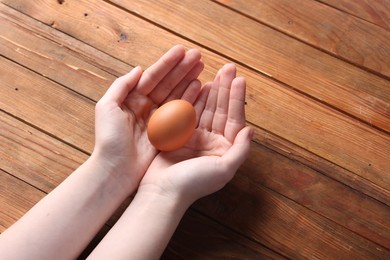 Photo of Woman with raw egg at wooden table, closeup