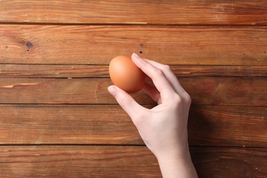 Photo of Woman with raw egg at wooden table, top view. Space for text