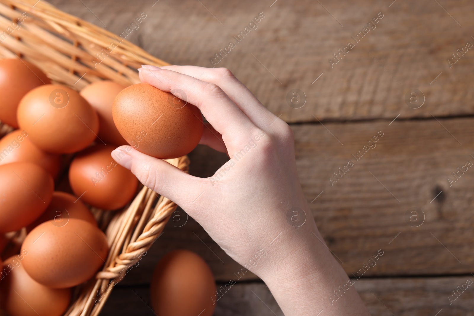 Photo of Woman with raw eggs at wooden table, top view. Space for text