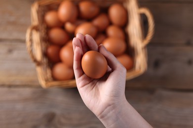 Photo of Woman holding raw egg above wooden table, top view