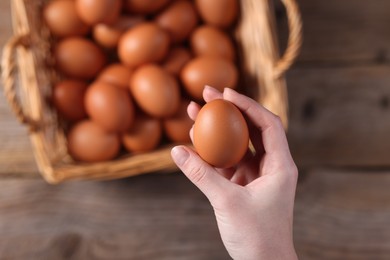 Photo of Woman holding raw egg above wooden table, top view