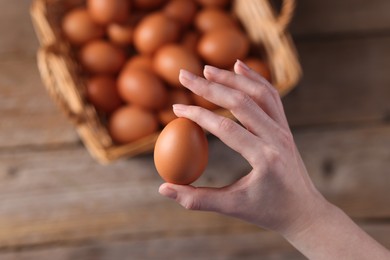 Photo of Woman holding raw egg above wooden table, top view