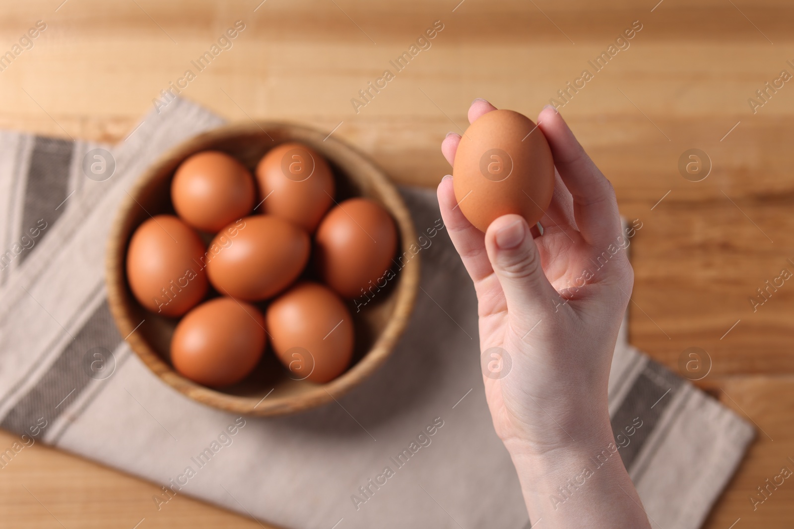 Photo of Woman holding raw egg above wooden table, top view