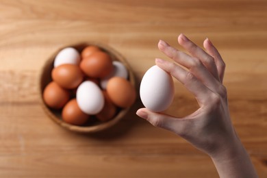 Photo of Woman with raw eggs at wooden table, top view