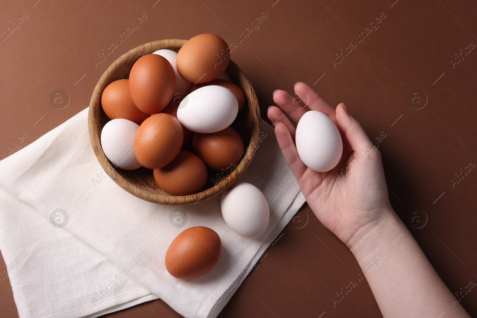 Photo of Woman with raw eggs on brown background, closeup