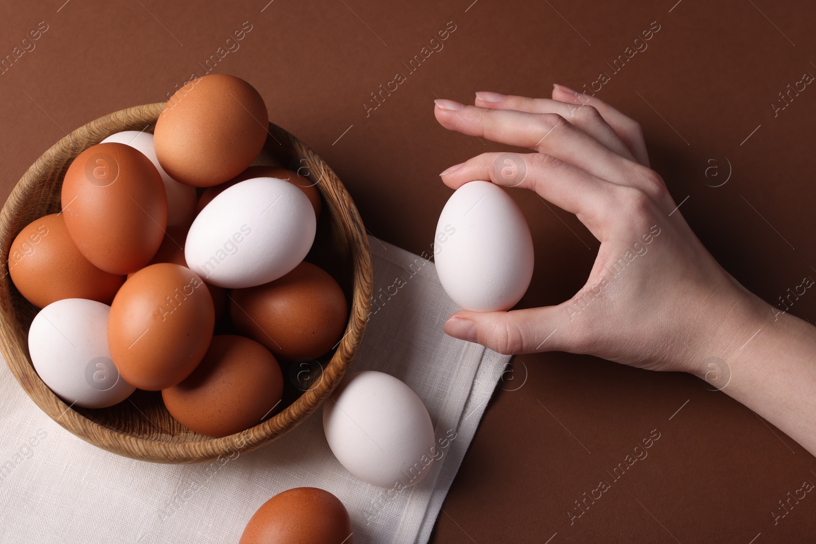 Photo of Woman with raw eggs on brown background, closeup