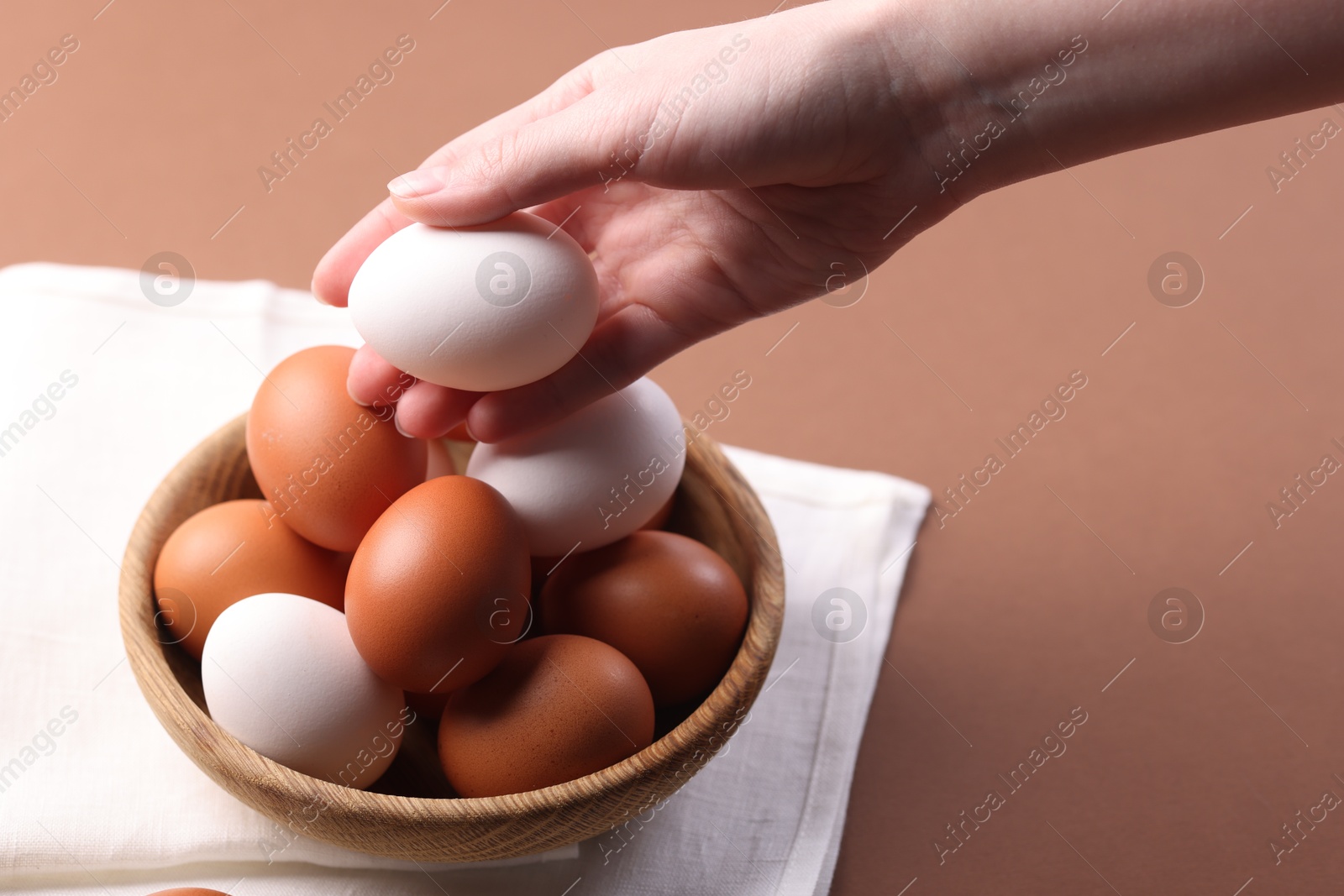 Photo of Woman with raw eggs on brown background, closeup