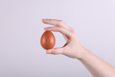 Photo of Woman holding raw egg on light background, closeup