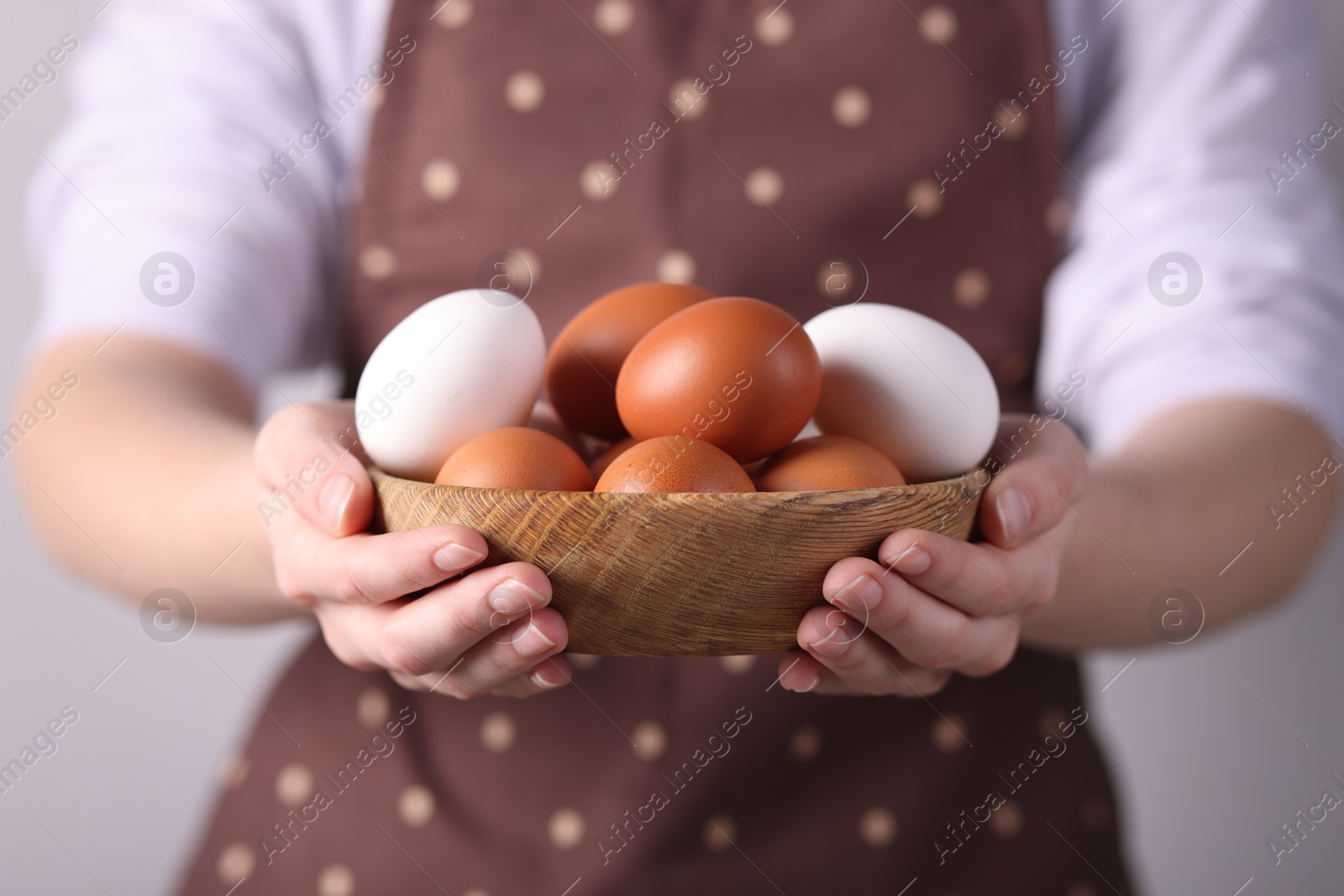 Photo of Woman with bowl of raw eggs on grey background, closeup