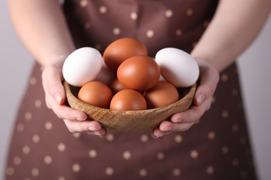 Photo of Woman with bowl of raw eggs on grey background, closeup