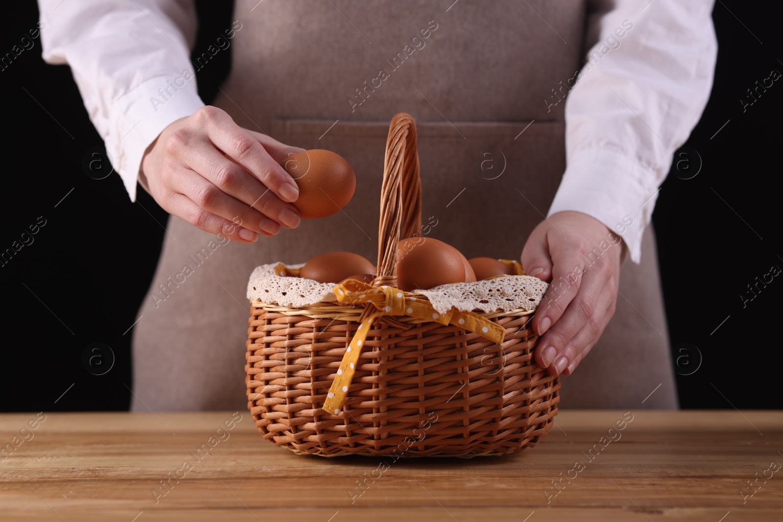 Photo of Woman with basket of raw eggs at wooden table, closeup