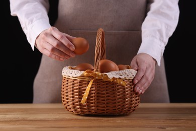 Photo of Woman with basket of raw eggs at wooden table, closeup