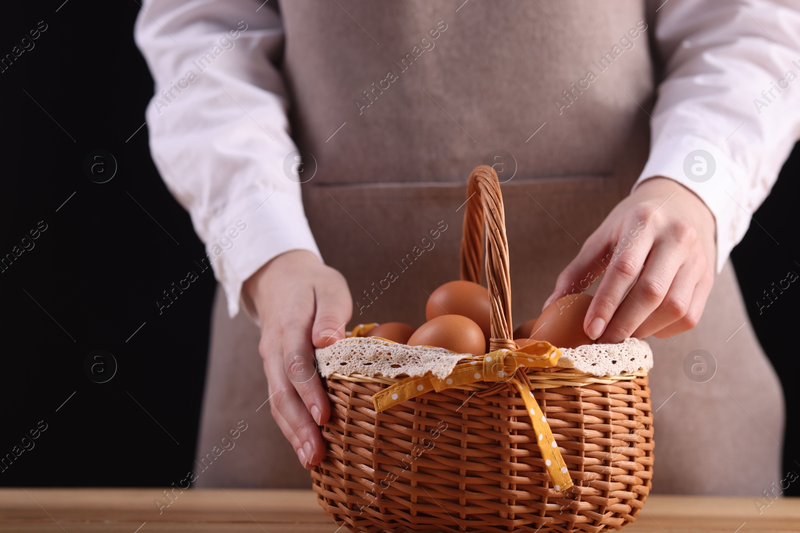 Photo of Woman with basket of raw eggs at wooden table, closeup