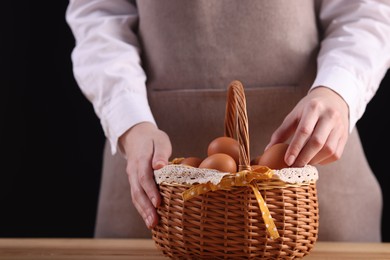 Photo of Woman with basket of raw eggs at wooden table, closeup