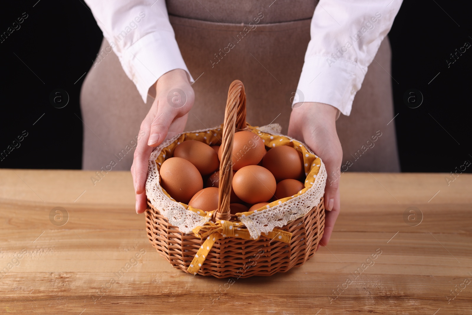 Photo of Woman with basket of raw eggs at wooden table, closeup