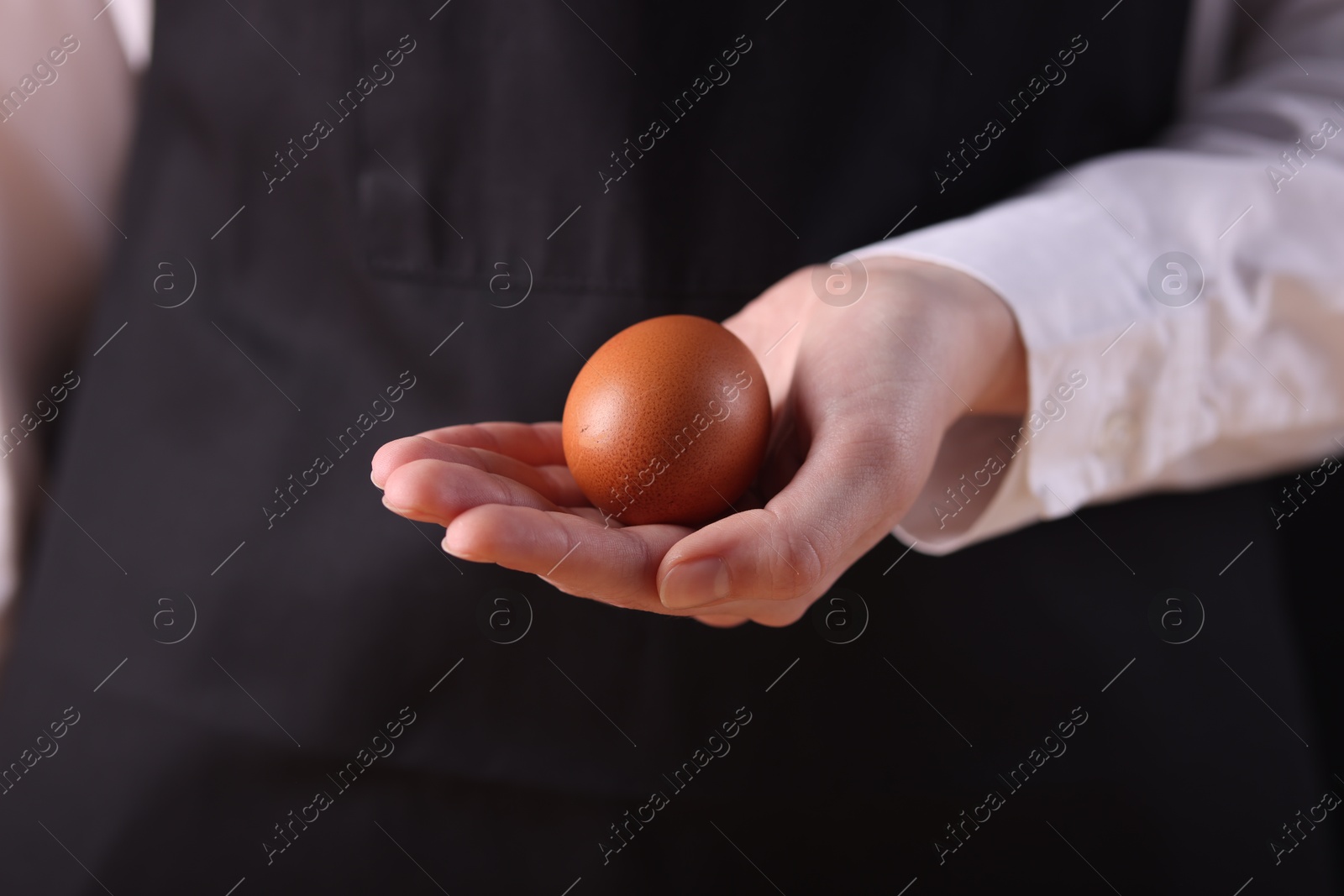 Photo of Woman with raw egg on dark background, closeup