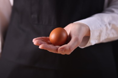 Photo of Woman with raw egg on dark background, closeup