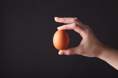 Photo of Woman holding raw egg on black background, closeup. Space for text