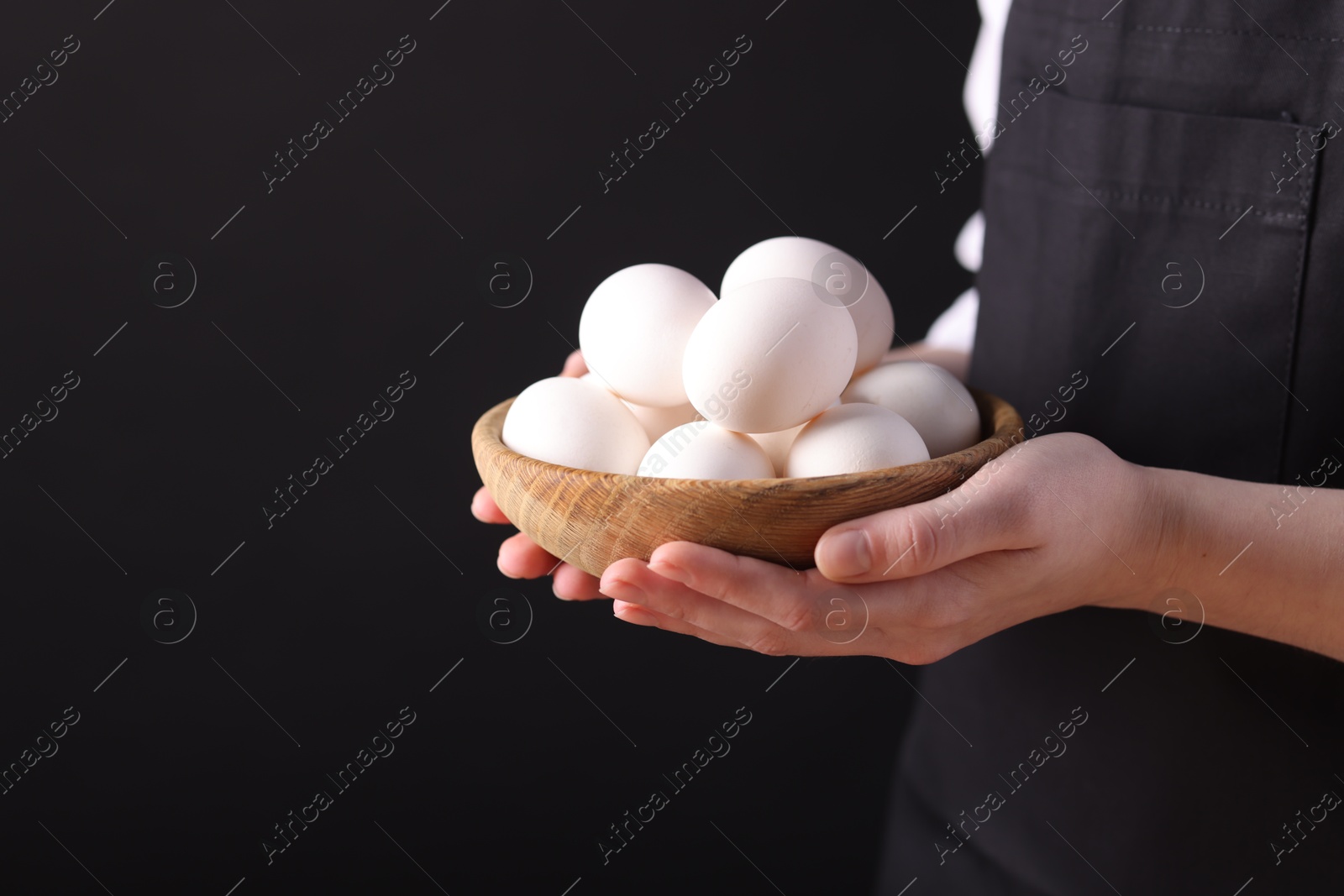 Photo of Woman with bowl of raw eggs on black background, closeup. Space for text