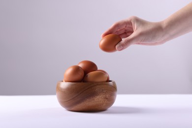 Photo of Woman taking raw egg from bowl at white table, closeup. Space for text