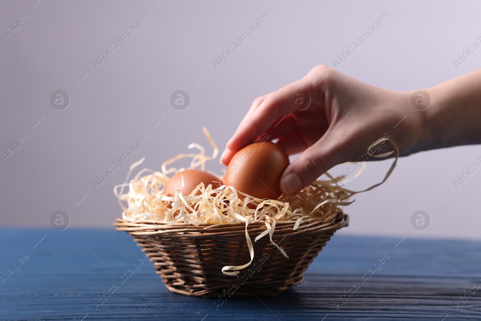 Photo of Woman with basket of raw eggs at blue wooden table, closeup. Space for text