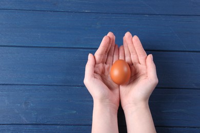 Photo of Woman holding raw egg on blue wooden table, top view. Space for text