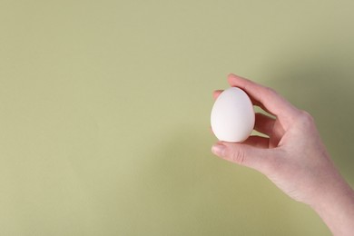 Photo of Woman holding raw egg on olive background, closeup. Space for text