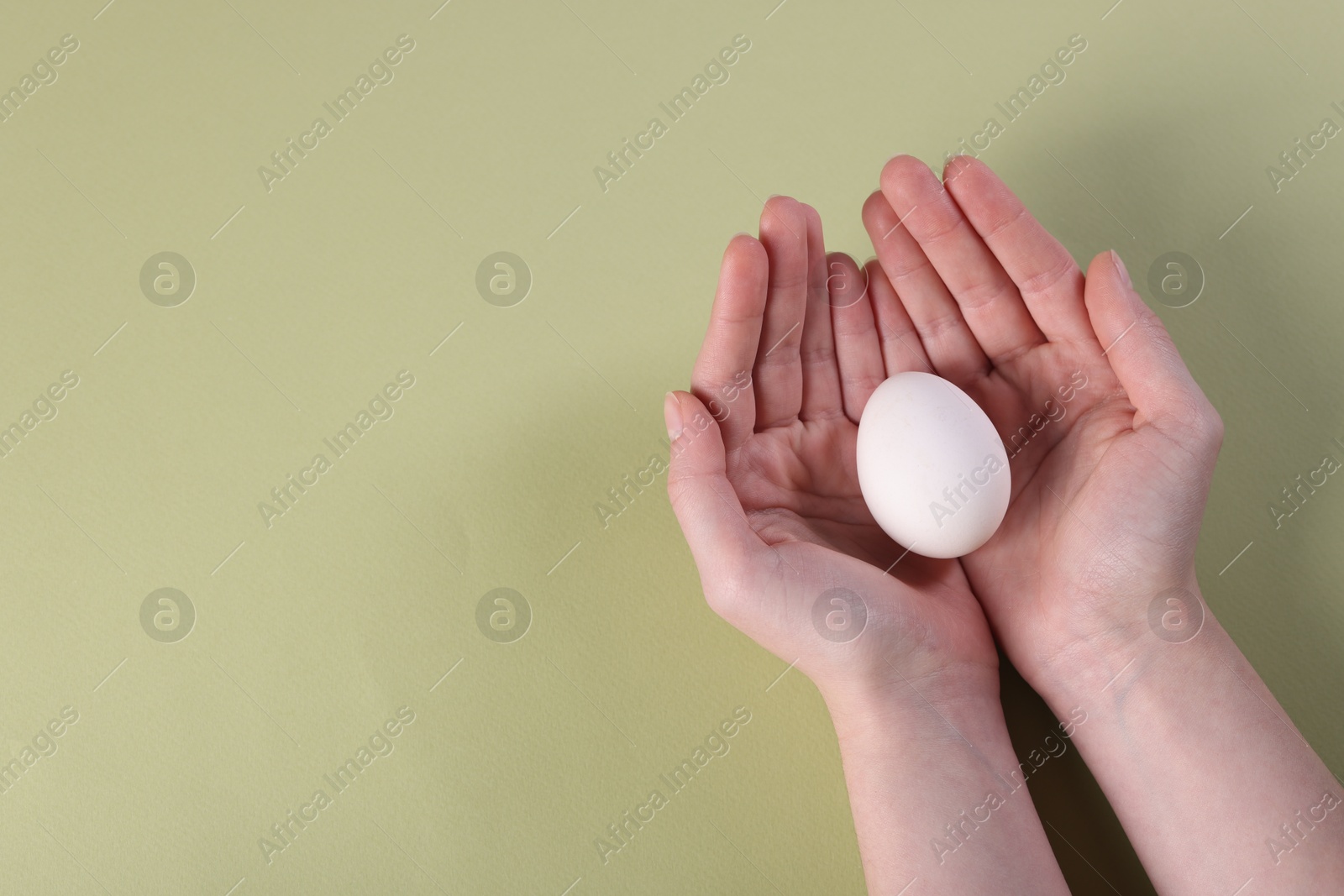 Photo of Woman holding raw egg on olive background, closeup. Space for text