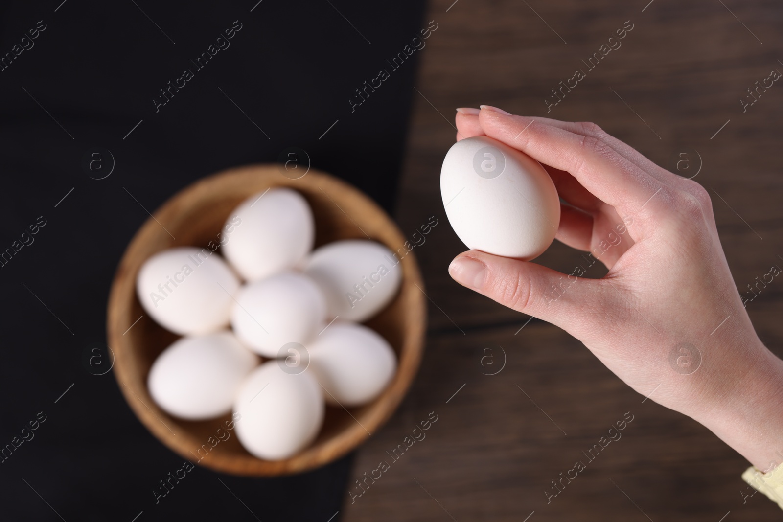 Photo of Woman holding raw egg over wooden table, top view