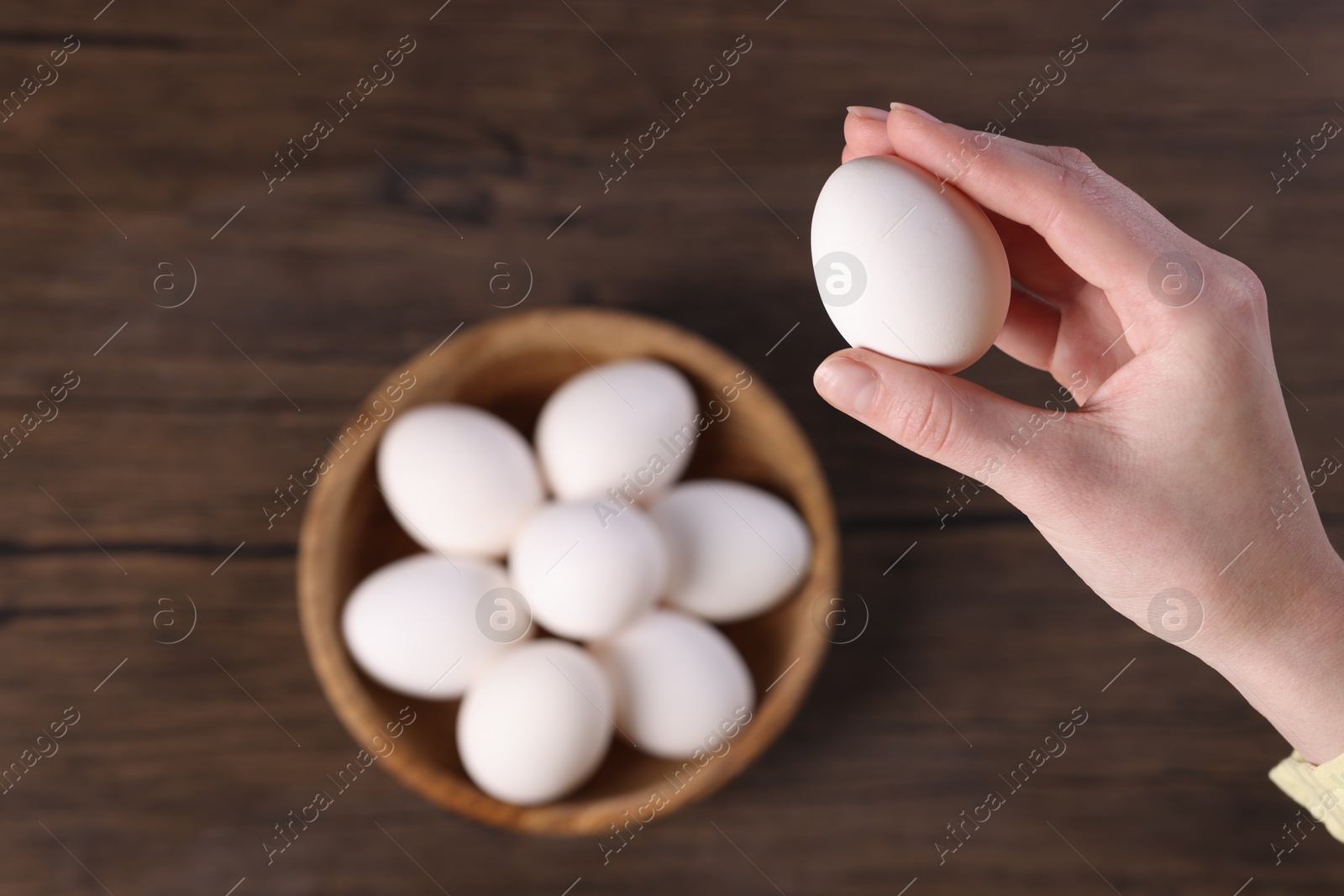 Photo of Woman holding raw egg over wooden table, top view