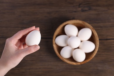 Photo of Woman holding raw egg over wooden table, top view