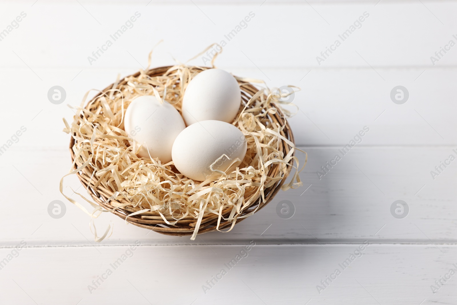 Photo of Raw eggs in basket on white wooden table, closeup